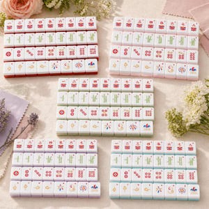 May include: A set of white mahjong tiles arranged in five rectangular grids. Each tile features colorful engraved symbols, including Chinese numerals, bamboo stalks, circular patterns, and directional markers, with the word JOKER on specific tiles.