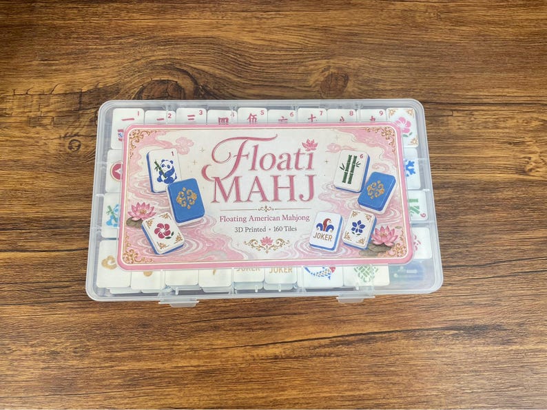 May include: A clear plastic storage case containing 160 white 3D printed American Mahjong tiles. The label on the lid features the text Floati MAHJ, Floating American Mahjong, 3D Printed, 160 Tiles, with illustrations of tiles showing a panda, bamboo, flowers, and a joker.