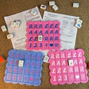 Puede incluir: Un juego de mesa con tableros rosas y azules, fichas y hojas de instrucciones. Los tableros rosas tienen el texto "RRR LLL", "AAAAAA", "LLLRRR" y los números "123". El tablero azul tiene un texto similar. También se ven fichas e instrucciones dispersas.