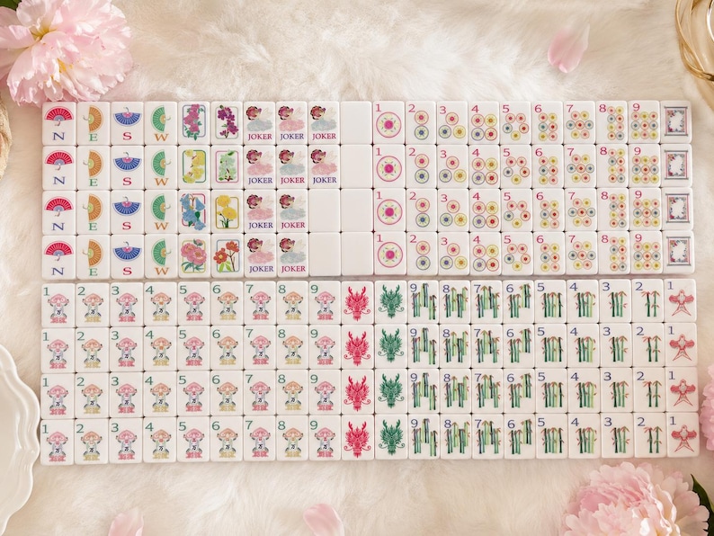 May include: A complete set of white Mahjong tiles, featuring various symbols, numbers, and characters. The tiles display illustrations of flowers, dragons, and jokers, with numbers from 1 to 9. The set is arranged on a soft, white surface.