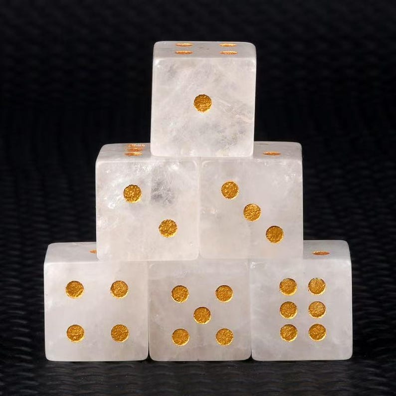 May include: Six clear quartz dice with gold-colored pips are stacked against a dark background. The dice are arranged in a pyramid shape, showcasing the different number combinations on each die. The dice are a game accessory.