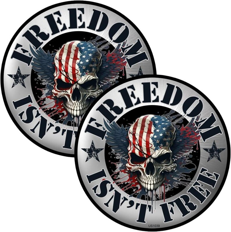 May include: Two round stickers with a skull design. The skull is painted with the American flag and has wings. The text "FREEDOM ISN'T FREE" is printed around the edge of the stickers.
