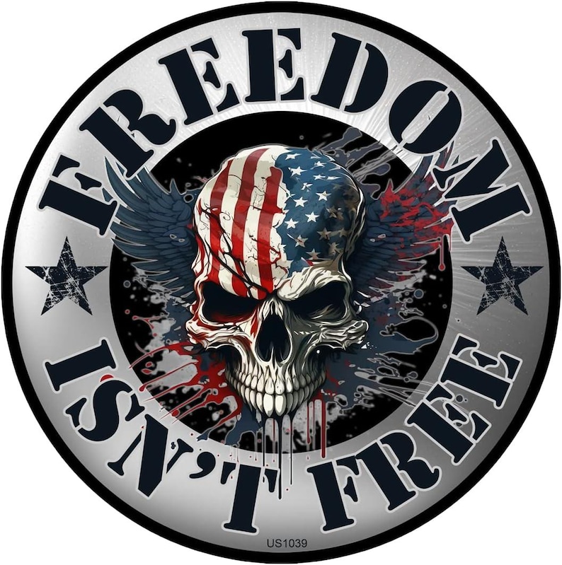 May include: A round, silver-colored graphic with the words "FREEDOM ISN'T FREE" encircling a skull. The skull is painted with the American flag design, with wings and blood splatter details. Two star shapes are on either side of the text.