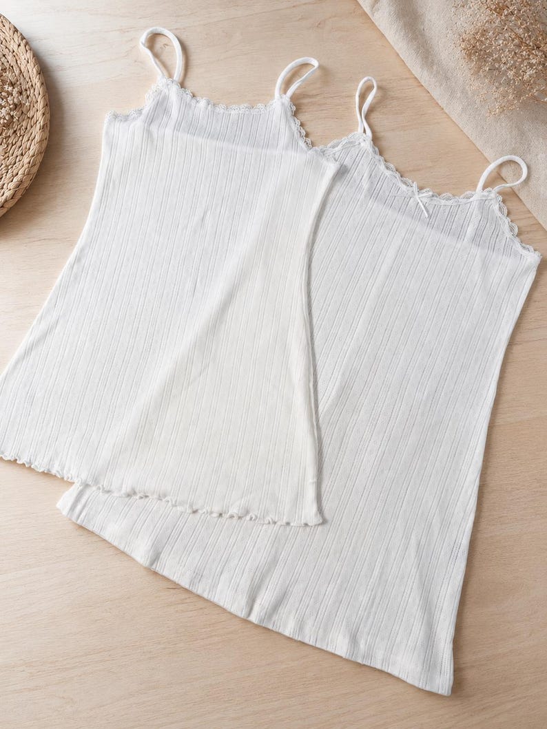 May include: Two white ribbed camisole tops with spaghetti straps and scalloped edges. The tops are made of a soft, lightweight fabric and are suitable for layering or wearing on their own. The camisoles are a versatile addition to any wardrobe.