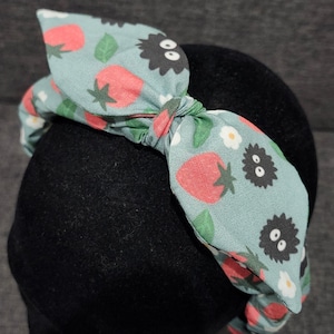 May include: A light blue headband with a bow featuring a pattern of strawberries, leaves, and black and white cartoon characters.