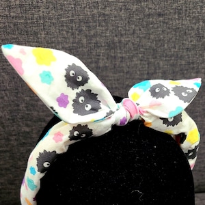 May include: White headband with a black and white print of cartoon characters. The headband is tied in a bow at the top.