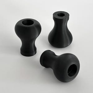 May include: Three black, rounded, decorative knobs with a smooth, matte finish. The knobs have a bulbous shape with a cylindrical base and a hole at the top. One knob is lying on its side, while the other two are upright.