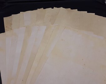 May include: A collection of rectangular sheets of paper arranged in a fan shape. Each sheet features a light beige, off-white, or cream colour with visible brown staining, spots, and aged textures across the surface of the paper material.