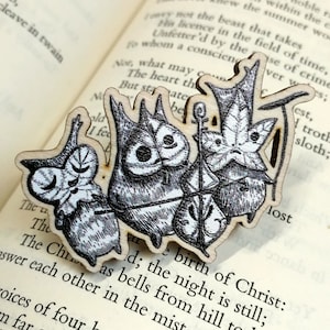 Op de afbeelding: Een houten bladwijzer met een zwart-witte illustratie van uilen en andere bosdieren. De bladwijzer is gevormd als een tak en heeft de tekst "The birth of Christ: the night is still." erop gedrukt.