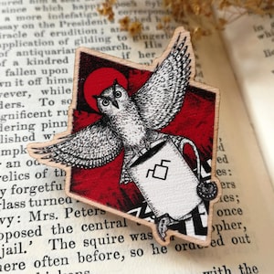 Könnte beinhalten: Ein Holz-Lesezeichen mit einer Schwarzweiß-Illustration einer Eule, die eine Tasse hält, vor einem roten Hintergrund. Der Text "THE INGOLDSBY LEGEND" ist im Hintergrund sichtbar.