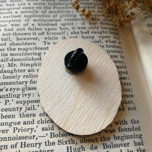 Pu&ograve; includere: Uno spillo nero e dorato con un designo in smalto nero. Lo spillo &egrave; appoggiato su un pezzo di legno con del testo sulla leggenda di Ingoldsby.