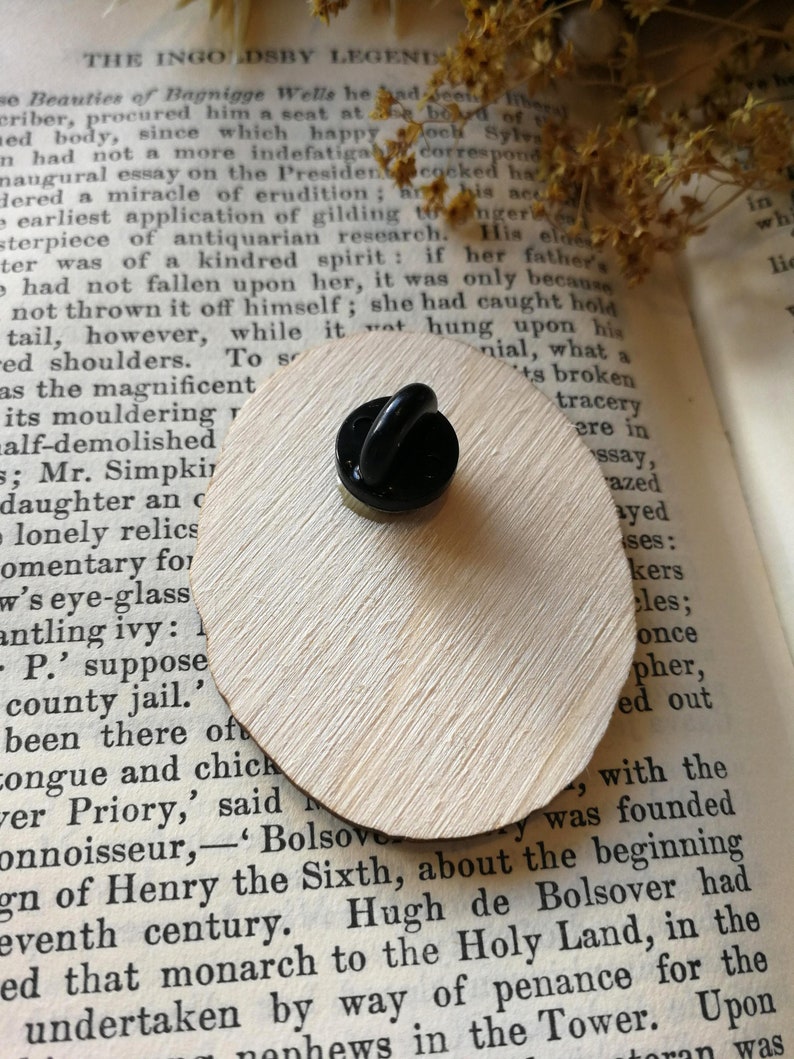 Pu&ograve; includere: Uno spillo nero e dorato con un designo in smalto nero. Lo spillo &egrave; appoggiato su un pezzo di legno con del testo sulla leggenda di Ingoldsby.