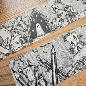 May include: Black and white illustrated washi tape featuring whimsical drawings of ghosts, pencils, keys, and other fantasy elements. The tape has a torn edge and is displayed on a wooden surface.
