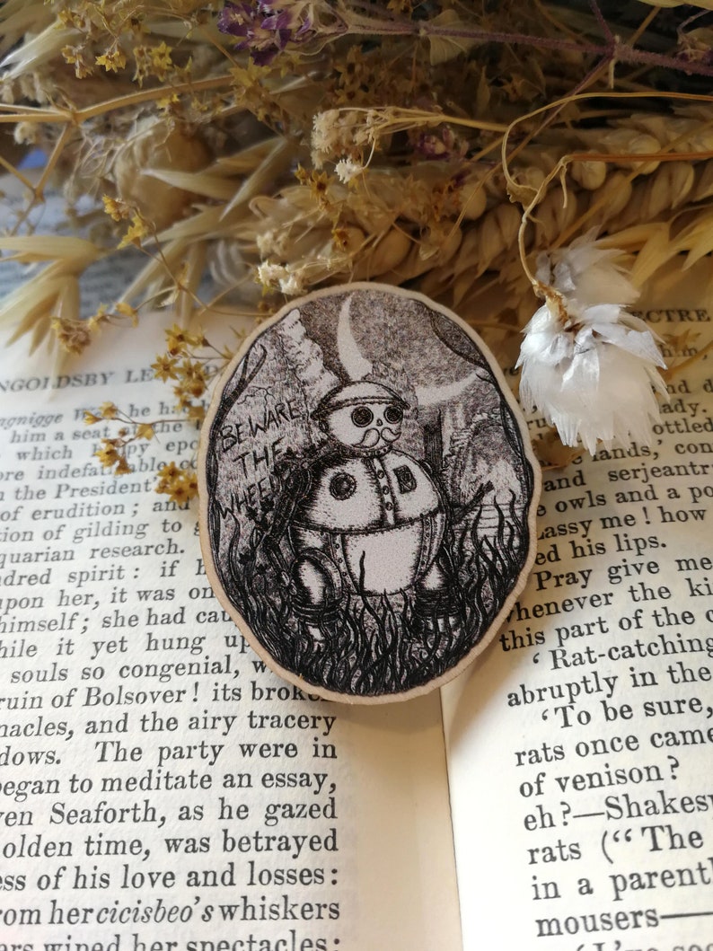 Pu&ograve; includere: Un'illustrazione in bianco e nero di una piccola creatura rotonda antropomorfa con una ruota come testa. La creatura indossa un cappello e ha i baffi. L'illustrazione &egrave; circondata da un bordo nero e si trova su uno sfondo bianco. Il testo "Beware the Wheel" &egrave; scritto sopra la creatura.