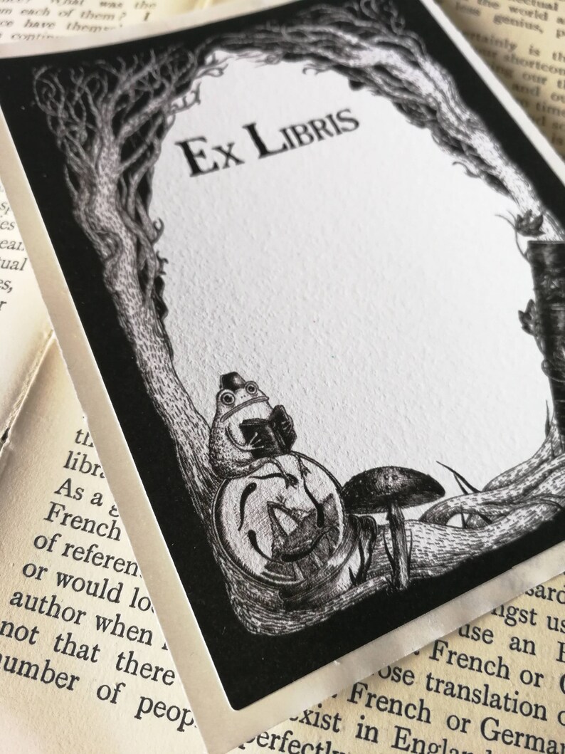 Op de afbeelding: Een zwart-witte exlibris met de tekst "Ex Libris" in een decoratief lettertype. Een kikker met een hoed en een boek zit op een paddenstoel onder een boom.