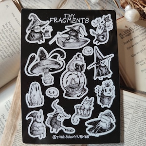 May include: A black sheet of stickers with a white border featuring various illustrations of whimsical creatures and characters. The stickers are on a black background and include a frog, a cat, a ghost, a mushroom, a skull, and a variety of other creatures. The text "Tiny Fragments" is at the top of the sheet. The text "@thisison turner" is at the bottom of the sheet.