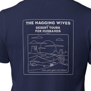 May include: Navy blue t-shirt with a white graphic on the back. The graphic reads "THE NAGGING WIVES DESERT TOURS FOR HUSBANDS" above a desert landscape illustration. The text "leave your quarrels behind" is at the bottom.