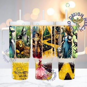 May include: Three white tumblers with handles and straws, each depicting a scene from The Wizard of Oz. The designs showcase characters such as the Wicked Witch, Tin Man, Lion, Dorothy, and the Yellow Brick Road. One tumbler has the text "We'll all see the"