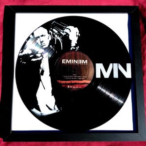 May include: Framed black vinyl record featuring a black and white image of Eminem. The record is labeled "Eminem The Eminem Show" and includes the letters "MN" in white. The frame is black and the background is white.
