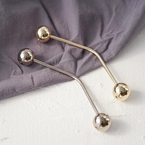 Pu&ograve; includere: Due spille a barra in metallo con estremit&agrave; sferiche. Una spilla &egrave; dorata, l'altra argentata. Le spille sono curve e poggiano su una superficie di tessuto grigio. Le spille vengono probabilmente utilizzate per fissare indumenti o accessori.