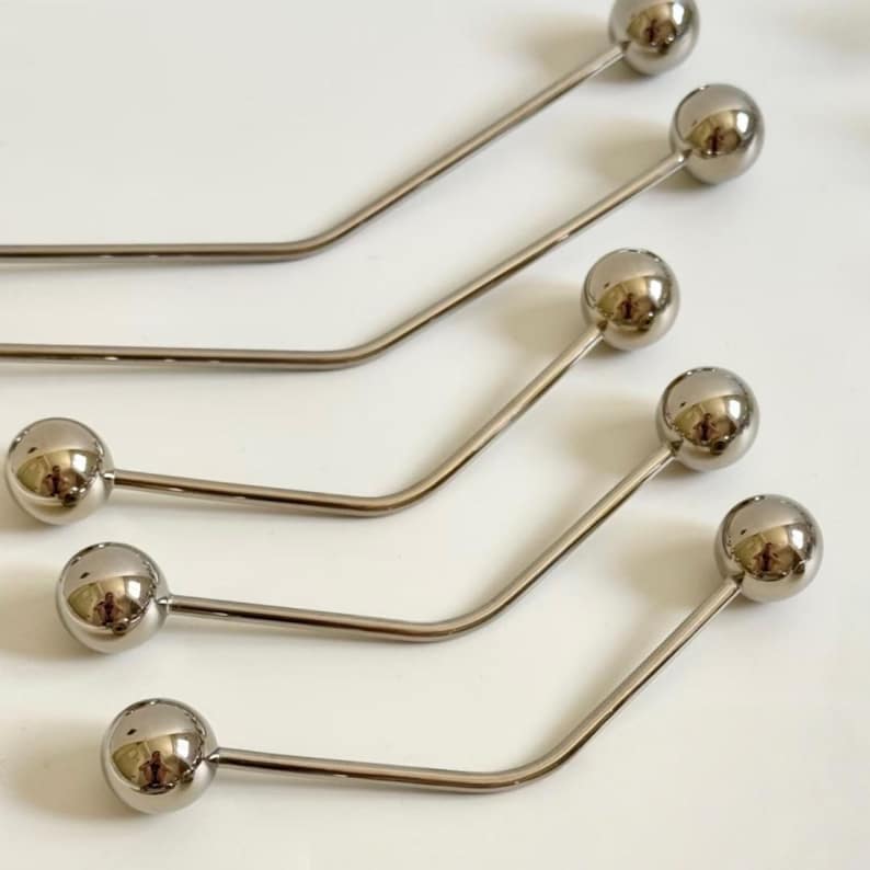 Pu&ograve; includere: Diversi strumenti in metallo color argento con una sfera a un'estremit&agrave; e un design curvo e angolato. Gli strumenti sono disposti in fila, con le sfere rivolte nella stessa direzione. Lo sfondo &egrave; una superficie bianca.