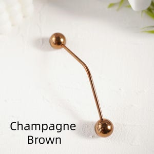 Pu&ograve; includere: Una spilla per hijab color marrone champagne con due estremit&agrave; sferiche. La spilla ha un design curvo e sottile. Il testo "Champagne Brown" &egrave; visualizzato in nero.
