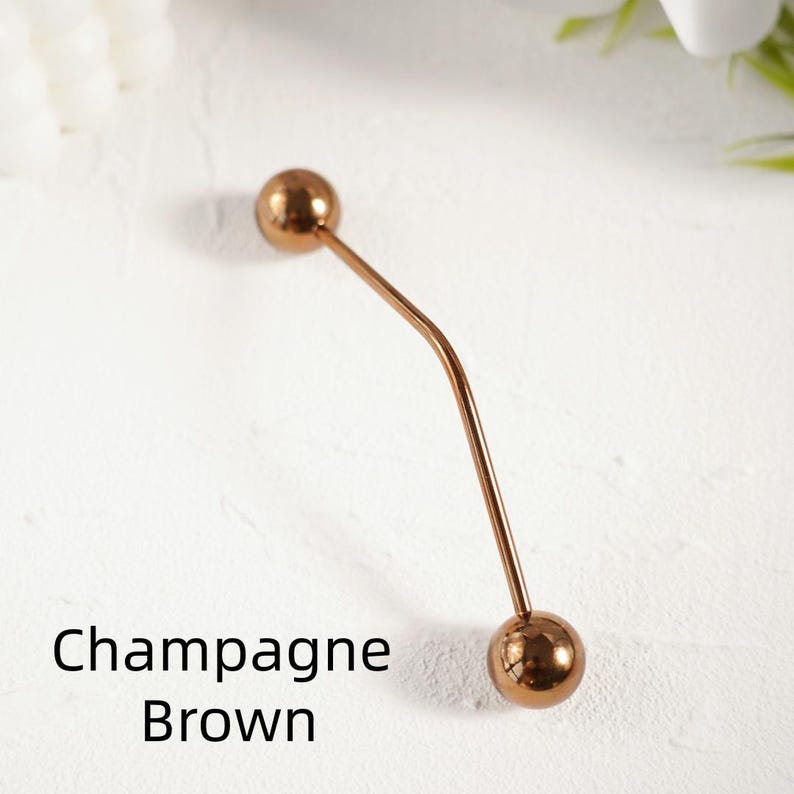 Pu&ograve; includere: Una spilla per hijab color marrone champagne con due estremit&agrave; sferiche. La spilla ha un design curvo e sottile. Il testo "Champagne Brown" &egrave; visualizzato in nero.