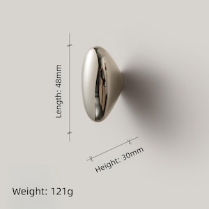 May include: A polished silver cabinet knob with an oval shape. The knob is 1.9 inches long, 1.2 inches high, and weighs 4.3 ounces. The reflective surface of the knob creates a mirror effect, reflecting the surrounding environment.