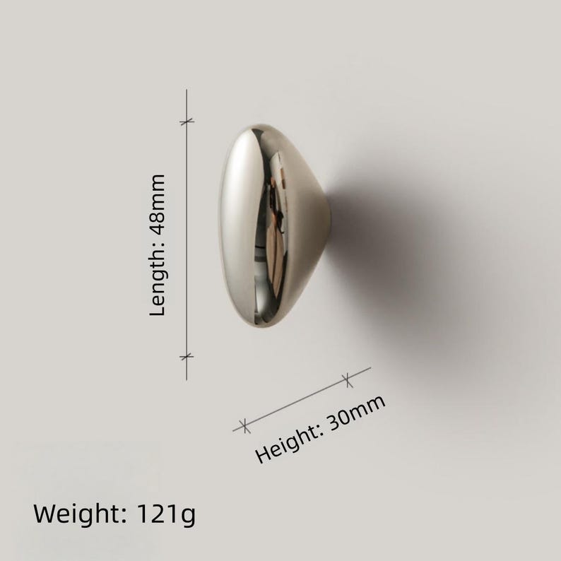 May include: A polished silver cabinet knob with an oval shape. The knob is 1.9 inches long, 1.2 inches high, and weighs 4.3 ounces. The reflective surface of the knob creates a mirror effect, reflecting the surrounding environment.