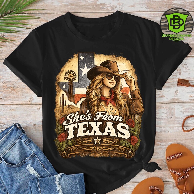 Peut inclure: T-shirt noir avec un motif d'une femme portant un chapeau de cow-boy et des lunettes de soleil, avec le texte "She's From TEXAS". Le motif comprend le drapeau am&eacute;ricain, un moulin &agrave; vent et des roses.