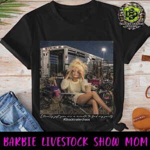 Puede incluir: Una camiseta negra con un estampado gr&aacute;fico de una mu&ntilde;eca rubia sentada en una silla plegable frente a un remolque de caballos, sosteniendo un vaso de pl&aacute;stico. El texto dice: Literally just give me a minute to find my sanity #Stocktrailerchaos.