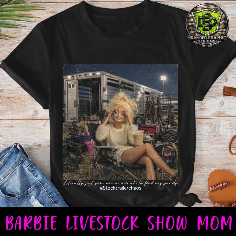 Puede incluir: Una camiseta negra con un estampado gr&aacute;fico de una mu&ntilde;eca rubia sentada en una silla plegable frente a un remolque de caballos, sosteniendo un vaso de pl&aacute;stico. El texto dice: Literally just give me a minute to find my sanity #Stocktrailerchaos.