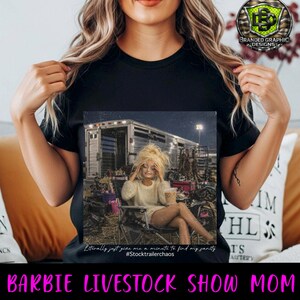 Puede incluir: Una camiseta negra con un estampado gr&aacute;fico de una mu&ntilde;eca de pelo rubio sentada en una silla plegable frente a un remolque de caballos. El texto debajo de la imagen dice: Literally just give me a minute to find my sanity #Stocktrailerchaos