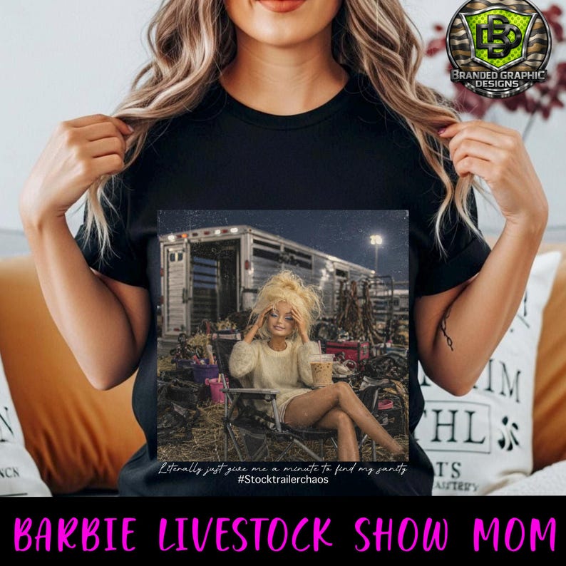 Puede incluir: Una camiseta negra con un estampado gr&aacute;fico de una mu&ntilde;eca de pelo rubio sentada en una silla plegable frente a un remolque de caballos. El texto debajo de la imagen dice: Literally just give me a minute to find my sanity #Stocktrailerchaos
