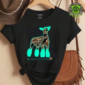 May include: Black t-shirt featuring a stylized lamb design with a camouflage pattern in brown, black, and tan. The lamb has turquoise accents and the text "It's Just A Lamb Thing" in turquoise. The shirt is from Shein.
