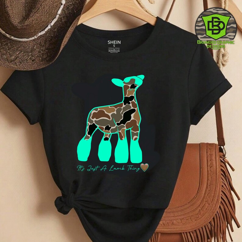 May include: Black t-shirt featuring a stylized lamb design with a camouflage pattern in brown, black, and tan. The lamb has turquoise accents and the text "It's Just A Lamb Thing" in turquoise. The shirt is from Shein.