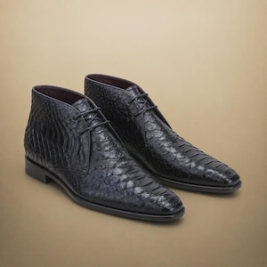 May include: A pair of black ankle boots featuring a textured snakeskin pattern. These boots have a lace-up closure with thin black laces, a rounded toe, and a low heel. The interior lining is a dark purple colour, and the soles are black.