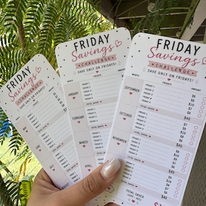 Może przedstawiać: Trzy białe karty „Friday Savings Challenge” z różowym i czarnym tekstem. Karty są trzymane w dłoni i zawierają narzędzie do śledzenia oszczędności dla każdego miesiąca, z miejscem na zapisywanie zaoszczędzonych kwot. Karty mają wzór serca.