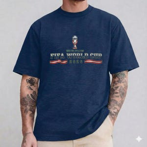 May include: Navy blue t-shirt featuring the FIFA World Cup 2026 logo. The design includes a trophy, a soccer ball, and the text "United States". The text "FIFA WORLD CUP 2026" is displayed in a bold, stylized font.