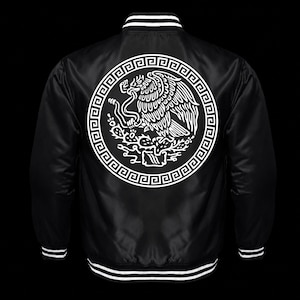 May include: A black varsity jacket featuring a white graphic on the back. The design displays an eagle perched on a cactus within a circular frame bordered by a Greek key pattern. The jacket has a ribbed collar, cuffs, and hem with white stripes.