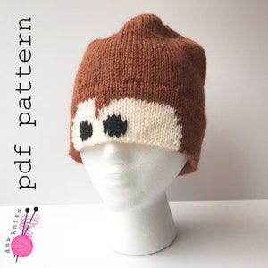 May include: A brown and white knitted hat with black eyes. The hat is on a white mannequin head. The text "pdf pattern" is written vertically on the left side of the image.