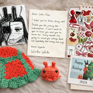 May include: An assortment of handmade items, including a crocheted hat with red and green floral patterns, a small orange crocheted creature, and a handwritten letter. The letter reads "Dear John Doe, I hope you've been doing well!"