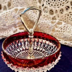 May include: A ruby red and clear crystal serving dish with a silver handle. The dish has a cut crystal design and a scalloped edge. The handle is arched and attached to the center of the dish.
