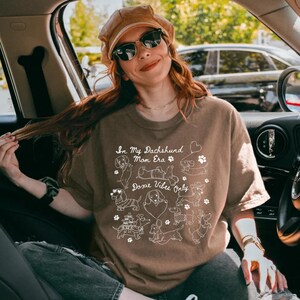 Espresso Comfort Colors® t-shirt featuring multiple dachshund illustrations with playful poses, hearts, and paw prints in a retro style design.