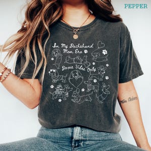 Pepper Comfort Colors® t-shirt featuring multiple dachshund illustrations with playful poses, hearts, and paw prints in a retro style design.