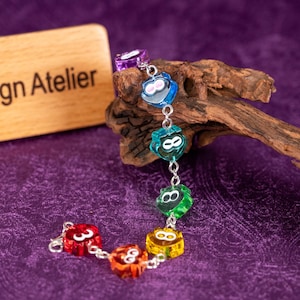 May include: A colorful bracelet featuring translucent, heart-shaped charms in various colors: purple, blue, green, yellow, and red. Each charm has a silver-colored number 8 or 3. The bracelet is displayed on a piece of wood against a purple background.