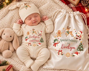 May include: A cream-colored ribbed long-sleeve baby bodysuit and matching knotted hat featuring a Christmas graphic with a reindeer, snowman, Santa, and tree, with text reading Evelyn's First Christmas 2026, next to a matching drawstring bag.