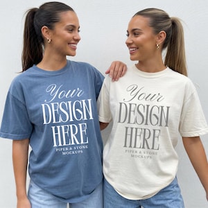 May include: Two short-sleeve crewneck t-shirts, one in dusty blue and one in off-white, each featuring the white or grey printed text "Your DESIGN HERE" followed by "PIPER & STONE MOCKUPS" in a serif font centered on the chest area.