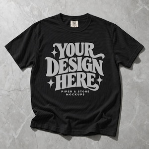 May include: A black short-sleeve t-shirt featuring the white text "YOUR DESIGN HERE" in a bold, stylized font with four-pointed star accents. Below the main text, smaller white text reads "PIPER & STONE MOCKUPS". The shirt has a crew neckline.