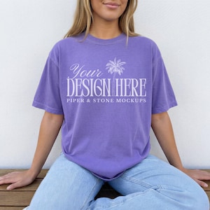 May include: A purple short-sleeve t-shirt featuring white text that reads Your DESIGN HERE and PIPER & STONE MOCKUPS, accompanied by a white palm tree graphic centered on the chest. The shirt has a crew neckline and a relaxed, loose fit.